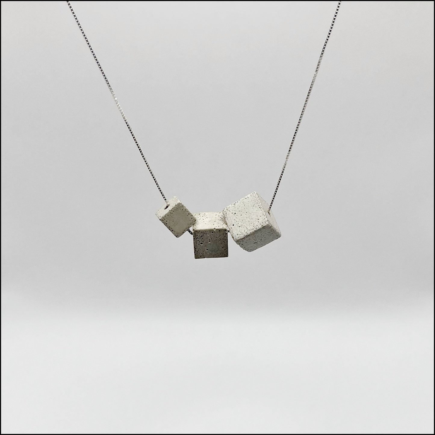 A silver 925 box chain necklace with three gray concrete cubes attached to it, displayed against a white background.