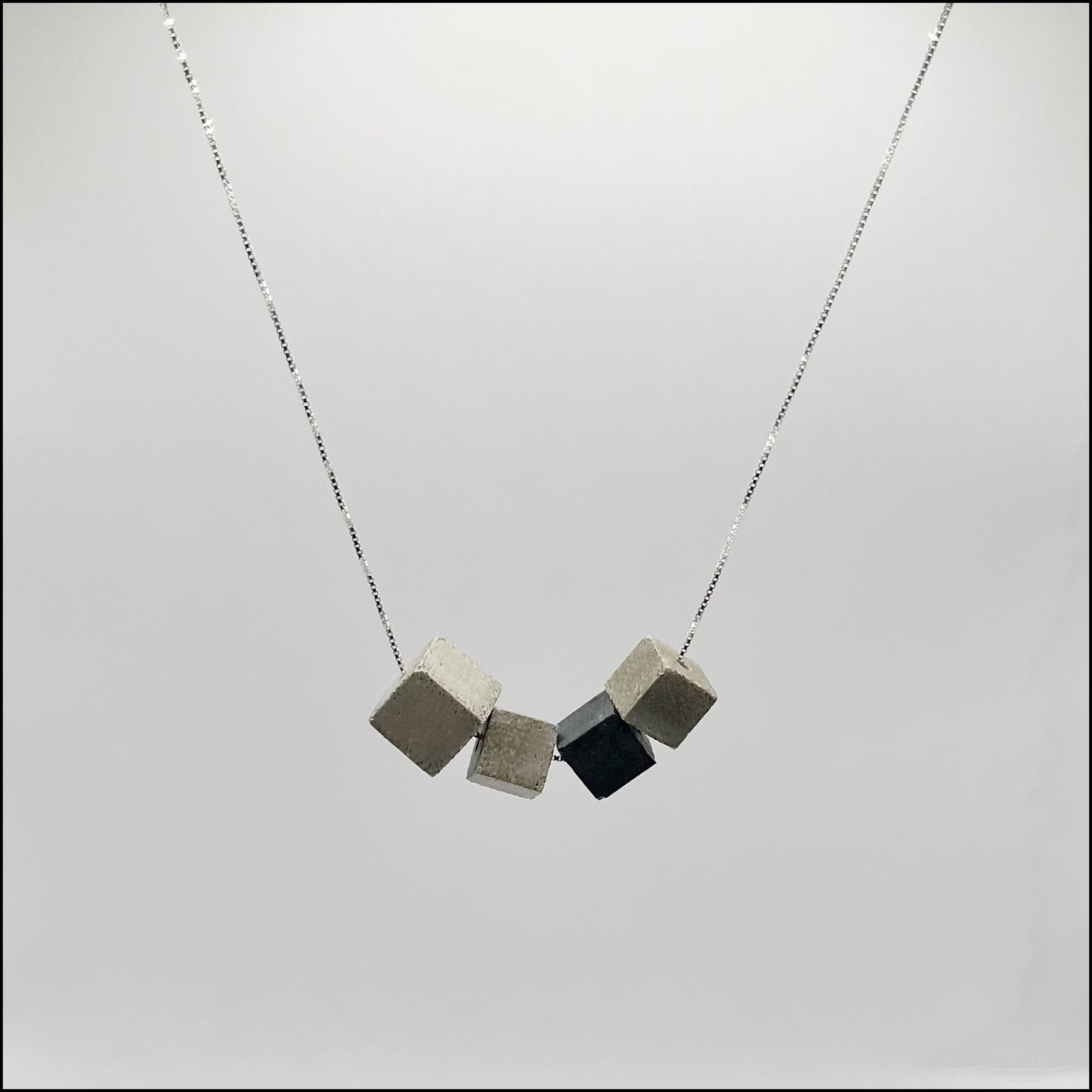 A silver 925 box chain necklace with four concrete cubes, including one larger cube and one in anthracite color, on a light background.