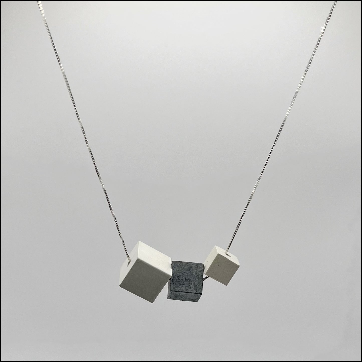 A silver box chain necklace with three concrete cubes in different sizes, attached to the chain.