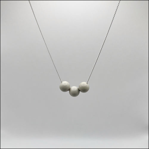 A silver curb chain necklace with three concrete spheres attached to it, displayed against a grey background.