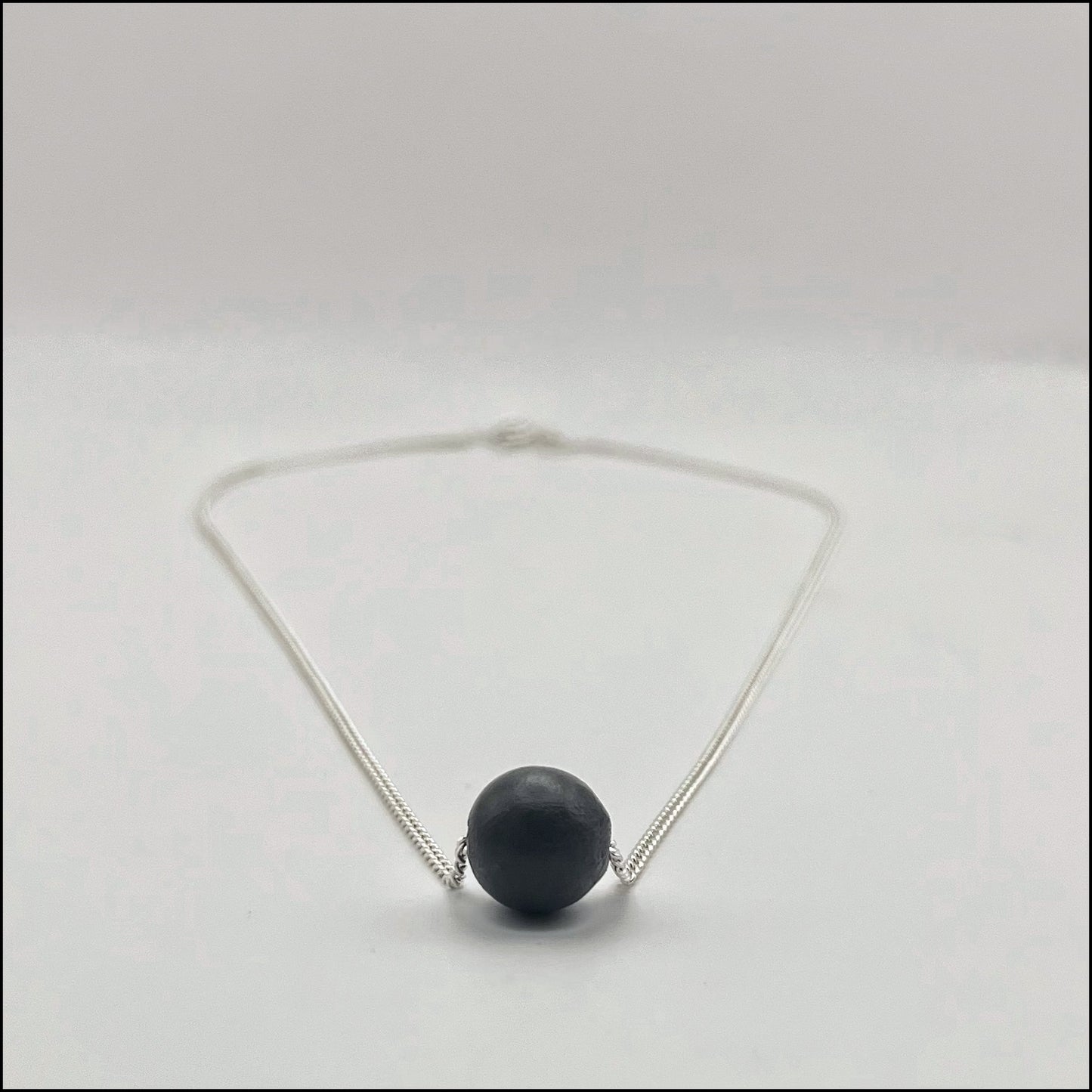 Necklace with a dark bead on a light gray background