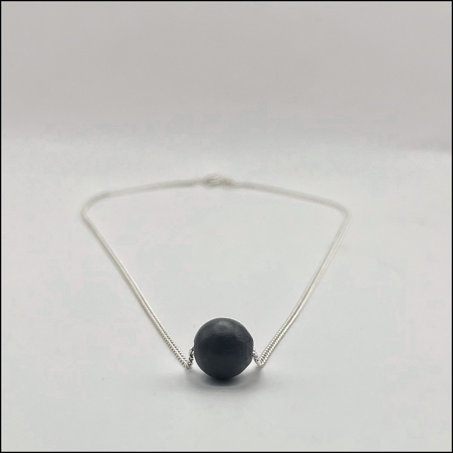 Necklace with a dark bead on a light gray background
