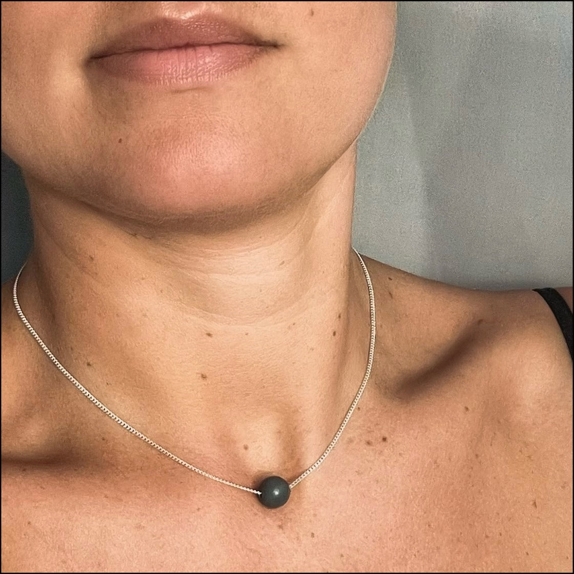 Close-up of a person wearing a necklace with a black pendant.