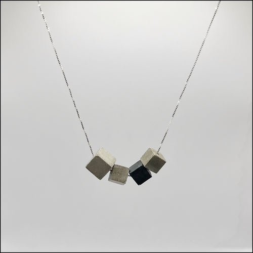 A silver 925 box chain necklace with four concrete cubes, including one larger cube and one in anthracite color, on a light background.
